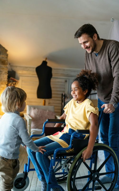 Happy multiethnic family. Smiling little girl with disability in wheelchair at home