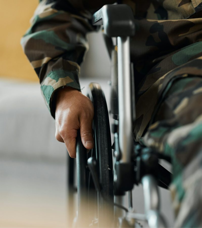 Man, hands and wheelchair in army from accident, war injury or healthcare support at hospital. Clos
